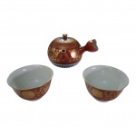 Bule em  e par de xícaras em porcelana japonesa, decoradas com dourado e azul sobre fundo ocre, uma das xícaras com bicado. Alt. 12, Diam. 11 cm.