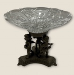 Extraordinária fruteira com base em metal espessurado a prata figuras de querubim sobre uma travessa em grosso cristal, medindo: 27 cm alt. x 32 cm diâmetro.