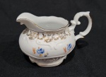 Antiga Leiteira em porcelana nacional da década de 1960, executado ao estilo francês do período Luís XV. Esmaltagem vítrea na cor branca, decorada com motivo vegetalista modelado em relevo na própria pasta, dotado de genorosos arremates em douradura, com frisos, faixas e guirlandas floridas; bojo elipsóide ornamentado, em ambas as faces, com flores em estampagem policromada, asa lateral em voluta coberta por folha de acanto, bico encurvado e bordas recortadas. Marca da manufatura no verso. Medindo 9 x 11.5 x 14.5 cm
