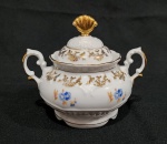 Antigo açucareiro em porcelana nacional da década de 1960, executado ao estilo francês do período Luís XV. Esmaltagem vítrea na cor branca, decorada com motivo vegetalista modelado em relevo na própria pasta, dotado de genorosos arremates em douradura, com frisos, faixas e guirlandas floridas; bojo elipsóide ornamentado, em ambas as faces, com flores em estampagem policromada, tampa campaniforme encimada por puxador com formato de concha estilizada, asa lateral em voluta coberta por folha de acanto, bordas recortadas. Marca da manufatura no verso. Medindo 12.5 x 11 x 14.5 cm