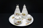 REAL (1943-1972) - Elegante galheteiro em fina porcelana branca, moldada na pasta, contendo 5 peças ornadas com rosas e folhagens em rica policromia e friso a ouro folha. Pega imitando labareda, Marcada no fundo. Sendo: 2 recipientes para azeite e vinagre, saleiro, pimenteiro e bandeja. Maior diâm. 21cm. (recipiente para vinagre com bicado na borda).
