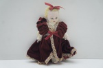 Antiga Boneca portuguesa confeccionada em pasta de biscuit, com vestes em veludo bordô. Alt. 17 cm.