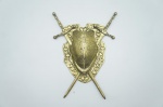 Panóplia decorativa (1), confeccionada em bronze cinzelado, adornada com couraça de armadura adornada com volutas e espadas entrelaçadas por baixo. Medidas: 26 x 19 cm.