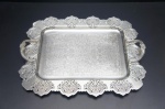 PRATA REGIA 90- Elegante bandeja confeccionada em metal espessurado à prata, formato retangular de extremos arredondados, centro levemente rebaixado adornado com motivo fitomorfo. Orla vazada e lavrada com motivos arabescos. Alças laterais em arco cinzelados em duplo enrolamento centralizado botão de flor. Marca da Manufatura no fundo. Medidas: 37 x 31 cm