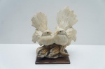 Escultura Capodimonte (Naples/Itália), representando um par de pombas (símbolos de paz e amor) ricamente detalhadas em sua plumagem, pousadas sobre adornos de espigas de milho (símbolos de colheita e fertilidade).A peça é marcada com um "N" sob uma coroa (indicativo de estilo Capodimonte, mas não da manufatura original do século XVIII) e é atribuída ao período do Século XX (anos 19501970). Apresenta acabamento em biscuit/resina com base escura, ideal para colecionadores de arte figurativa clássica italiana. Medidas: