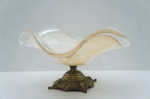 Suntuoso Centro de Mesa Antigo em Bronze Cinzelado e Vidro Artístico (Estilo Murano)Uma peça de coleção espetacular, este Centro de Mesa conjuga a opulência do metal antigo com a delicadeza do vidro artístico. A Base (Pé) é em bronze maciço e pesado, com um rico trabalho de entalhe e cinzelamento em estilo que remete ao Vitoriano/Art Nouveau, apresentando motivos florais em alto-relevo. A Taça (Bowl) é confeccionada em vidro artístico (estilo Murano), com formato orgânico ondulado. O vidro possui uma bela mistura de tons âmbar (ou coral) e branco-leitoso, com a técnica bulicante (aspecto marmorizado/esfumaçado), criando um efeito visual deslumbrante. A pátina do bronze atesta sua antiguidade. Peça em excelente estado de conservação, ideal para colecionadores.Características: Base em Bronze Maciço / Taça em Vidro Artístico (Estilo Murano). Medidas: Alt. 22 x Diâm. 41 cm.