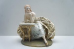 Guido Cacciapuoti (1892-1953)- Graciosa Escultura de porcelana italiana, manufatura "Capodimonte" em rica policromia representando "Une Dame" apoiada sobre mesa com volumoso vestido adornado com volutas e motivos à ouro folha. Medidas: 30 x 20 x 31 cm.