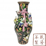 QIANLONG - CHINA - Magnífico e raríssimo vaso oriental em porcelana esmaltada, no estilo Famille Rose, ricamente ornamentado com motivos florais policromados sobre fundo preto. A peça apresenta figuras infantis em relevo, em trajes tradicionais, distribuídas de forma lúdica ao redor do corpo, símbolo de prosperidade e felicidade. Um laço cor-de-rosa modelado em alto-relevo adorna o centro da composição, conferindo delicadeza e movimento. A obra segue o refinado estilo difundido durante o reinado do imperador Qianlong (século XVIII), período áureo da porcelana chinesa, notável pela exuberância cromática e pela minuciosa execução artesanal. Mede 37 cm de altura x 10 cm de diâmetro da borda.