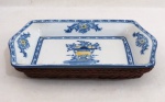 MADE EXCLUSIVE BANANA COLLECTION - Petisqueira retangular em porcelana esmaltada e vitrificada provavelmente Portuguesa de Alcobaça, decoração em azul e amarelo, com arranjos de flores, suporte em vime trançado que confere belo acabamento a peça. Med. 4 x 27 x 16 cm.