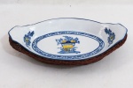 MADE EXCLUSIVE BANANA COLLECTION - Travessa oval formato navete em porcelana esmaltada e vitrificada provavelmente Portuguesa de Alcobaça, decoração em azul e amarelo, com arranjos de flores, suporte em vime trançado que confere belo acabamento a peça. Med. 5 x 25 x 14 cm.