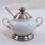 RIVA- açucareiro em porcelana branca com alças laterais, base, tampa e colher em metal espessurado a prata. Med. 11 x 14 cm.