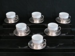 Conjunto com seis xícaras para café em porcelana branca decorada com frisos prateados. Acompanha seis suportes em metal prateado marcado Wolff.