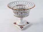 ROSENTHAL- Belíssima fruteira avarandada fenestrada na lateral em fina porcelana vitrificada, decorada na base e interior com rosas, filetada a ouro, base quadrada, coluna circular. Marcada na base. Med. 24 x 25 cm diâmetro.