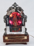 Antiga Capela portuguesa com Nossa Senhora de Fátima e o três pastorinhos, em madeira revestida em galalite perolado, tampa decorada com aplicações de guirlandas em metal espessurado a prata. Interior com nove micro lâmpadas  funcionando. O dispositivo musical requer revisão. Med. 30 x 18 x 10 cm.