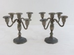Par de candelabros em metal espessurado a prata para cinco velas, base redonda moldada, coluna alongada com quatro braços curvos, terminando em bobeche. Prateação no estado. Med. 20 x 23 cm.