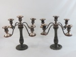 Par de candelabros em metal espessurado a prata para cinco velas, base redonda, coluna alongada e facetada, podendo usr como castiçal, encimado por quatro braços curvos terminados em bobeche. Med. 33 cm alt. Desgaste no prateado, VENDIDO NO ESTADO.