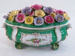 VISTA ALEGRE-  Grande caixa oval em porcelana portuguesa policromada no tom verde esmeralda, galeria central decorada com flores  frisos a ouro. Tampa adornada com flores em relevo, moldadas em guirlandas. Alças laterais com concheados. Apoiada sobre quatro pés. Med. 20 cm altura x 31 cm  x 16 cm .
