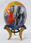 ARTE AFRICANA-um (1) ovo de avestruz , pintado à mão, com temática de caçada africana elefante, leopardo, leão, rinoceronte e búfalo, apoiado em base tripóide de dente de javali. Med. 24 cm altura.