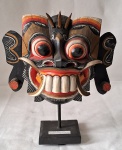 Imponente máscara balinesa representando o Deus dos Espíritos "Barong" em madeira ricamente entalhada e policromada. . O Barong é um Deus protetor da ilha de Bali, na Indonésia, e está relacionado às forças do bem. Amuleto para afugentar os maus espíritos. Existem diversas representações do mesmo nas regiões de bali. Podem representar cinco animais: Javali, tigre, dragão, serpente ou leão que é a forma mais comum, e é a utilizada na máscara acima. Med. 32 cm alt  28 cm diâmetro. Acompanha pedestal.
