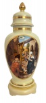 Palaciano potiche em porcelana esmaltada em tom marfim, com tampa em formato de pináculo e densas faixas em vibrante ouro. Em destaque, uma rica cena do renascimento representando a Natividade com expressivo jogo de luz e minucioso detalhamento das figuras. A composição evoca a tradição renascentista, evidenciando traços artísticos que valorizam a peça como objeto de contemplação e devoção. No verso ramalhete de flores em rica policromia.  Mede 47cm.