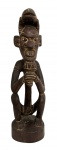 ÁFRICA - Singular escultura artesanal em madeira maciça, representando figura antropomórfica em posição de vigília, com expressivo semblante e traços rústicos que ressaltam o caráter primitivo e ritualístico da peça. Os detalhes esculpidos à mão, incluindo ornamentos na cabeça e nas mãos, evidenciam a força simbólica e a tradição cultural de arte tribal africana.Acabamento em tom natural escuro, com pátina suave que realça as texturas e o entalhe minucioso.Dimensão: 51 cm de altura.Uma obra que une a força da ancestralidade ao charme do artesanato étnico, perfeita para colecionadores e amantes de arte primitiva e decoração de interiores