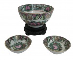 Conjunto de três tigelas em porcelana chinesa "Famille Rose", finamente decoradas à mão com flores, pêssegos e símbolos de longevidade, em policromia sobre fundo branco. Borda realçada em dourado. A maior acompanha base em madeira entalhada.Período: início do século XX. Medida do maior 11cm de diâmetro.