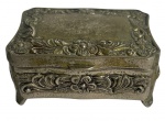 Delicada caixa antiga em metal prateado, ricamente trabalhada com relevos florais em estilo rococó. Interior revestido em veludo escuro. Peça de delicado encanto decorativo, ideal para joias, relíquias ou composições de época. Mede 8cm x 5,5cm.