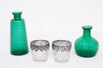 Lote constando de quatro peças decorativas diversas sendo duas jarras de formas diferentes em vidro moldado no tom verde esmeralda - med. 15x10 cm de diâmetro na base (com imperceptível bicado na borda) e med. 23x10 cm de diâmetro na base (a maior), e dois porta velas em vidro moldado com pátina prateada e guarnição da borda em metal - med. 9,5x9 cm de diâmetro na borda (guarnição com pequenos defeitos)