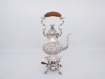 Elegante Samovar em metal espessurado a prata, ricamente cinzelado e guilhochado com flores, volutas e arabescos, tampa com pega na forma de pinha, alça curva com pega em madeira, apoiado sobre base com quatro pernas com pés na forma de conchas, parte inferior central com queimador e alça em madeira - completo - Samovar com banho em perfeito estado - med. 38x22x15 cm medida com alça em pé - med. 47x22x15 cm