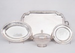 Lote constando de quatro antigas peças em metal espessurado a prata da manufatura "Wolff", sendo uma imponente bandeja com alças, bordas recortadas, ricamente cinzeladas com frisos, flores e folhagens, marca da manufatura na base med. 77x44 cm e parte de conjunto de baixela, sendo uma sopeira com pega da tampa na forma de pinha com bordas, alças e base cinzeladas com frisos, flores e folhagens med. 22x32x26 cm (parte interna com arranhões do uso), uma travessa redonda med. 30 cm de diâmetro e uma travessa oval med. 42x30 cm (com marcas de uso).