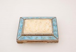 Antiga e elegante Trusse (caixa de porta pó de arroz) Italiana em prata contrastada teor 800 mile, tampa com placa esculpida em marfim representando "querubins", laterais decoradas com esmalte no tom azul Turquesa, laterais e fundo cinzelado com flores e volutas, parte interna com espelho em cristal bisotado e banho de ouro med. 18,5x7 cm. Peça para colecionadores.