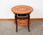 Mesa auxiliar estilo francês, tampo oval marchetado com decoração flores, folhagens e volutas, borda com gradil em metal vazado, uma gaveta central com puxador em metal, pernas curvas e prateleira inferior com guarnições em metal, uma prateleira na parte inferior marchetada med. 63x47x33 cm (com pequenos desgastes no verniz).