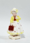 Estatueta em porcelana alemã, policromada, com marca da manufatura Katzhutte, representando menina com maleta. Apresenta numeração em crio na base.  Alt. 22cm.