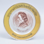 Prato decorativo de porcelana comemorativo ao primeiro centenário de Frédéric Chopin (1849 - 1949, traz assinatura artistica e citação "VIVO NUM SONHO E DURMP DURANTE MINHAS VIGÍLIAS". Verso numerado e marcado porcelana P II. 25 cm diam