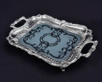 Bandeja retô estilo vitoriana. Composição de vidro com decoração satine e cercadura de metal prateado com relevo de concheados, gomos e arabescos. Apresenta ainda 4 pés de folhas de acanto. 50x31x7 cm