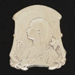 METAL PRATEADO, uma (1) pequena placa retratando busto feminino perfilado com flores em torno, período ArtNouveau, assinada TAIPAC, medindo 6 x 5 cm, vide foto.