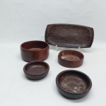 Cinco petisqueiras em madeiras diversas; 4 redondas e 1 retangular. Uma redonda com quebrado na borda e bandeja rachada. Maior redonda Alt. 7 x Diam. 14cm e retangular 29 x 14cm.