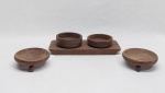Cinco peças em madeira, duas petisqueiras com pés trípode na forma de esferas, duas petisqueiras redondas e bandejinha retangular com dois nichos redondos. Med. 10 a 27 cm.