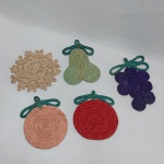 Cinco descansos para pratos quentes em sisal, na forma de frutas e flores. Med. 19 a 22 cm.