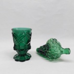 Duas peças em vidro verde: Garrafa na forma de cacho de uva (rachadura na boca) e copo moldado com losangos e pingentes no bojo. Alt. 7 e 13 cm.