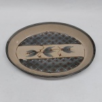 Travessa oval em cerâmica esmaltada na cor marrom, borda acinzentada e fundo decorado com flores e losangos pintados a mão. Med. 28 x 20 cm.