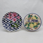 Dois pratos redondos para servir em porcelana policromada: A) "EL PRIMO", decorado com limas, flores e folhagens pintadas a mão. Diam. 25 cm. B) Decorado com orquídeas, lascado na borda. Diam. 27 cm.