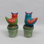 Duas floreiras em barro cozido na forma de pássaros. Acompanha bases em porcelana com pátina verde. Um das floreiras com a base colada. Alt. 16 cm.