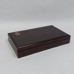 Caixinha em madeira escura, aplicada com brasão metálico da Marinha Chilena. Med. 3,5 x 19,5 x 11,5 cm.