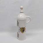 Garrafa c/ alça e tampa em porcelana branca decorada com diversos brasões coloridos. Pequeno lascado na tampa e desgaste na douração da base. Marcado WEISS. Alt. 26,5 cm.
