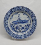 Prato decorativo em porcelana azul e branca. Borda decorada com flores e acantos, ao centro porta-aviões e brasões militares. Com as inscrições: "NAeL Minas Gerais - Verolme Estaleiros Reunidos vos desejam uma boa viagem". Diam. 35 cm.