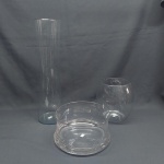Três peças em vidro translúcido: A) Duas floreiras, oval e cilíndrica. Alt. 19 e 2 cm. B) centro de mesa redondo. Med. 10 x 20 cm.