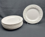 Oito (8) pratos rasos confeccionados porcelana branca, moldados na pasta. Adornado na borda com frutos e folhagens em relevo. Diâm. 26 cm. (3 pratos com bicado).