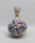 PORTO CARVALHINHO (1841-1960) - Garrafa com rolha de roscar confeccionada em faiança portuguesa do norte, séc. XX. Corpo bojudo, adornado em tons de azul e vinoso sobre fundo branco craquelê com enrolamentos vegetalistas e volutas com inscrição ao centro "BOTA-PATODOS". Pintada a mão. Marcada no fundo. Marcas do tempo. Alt. 21,5 cm.