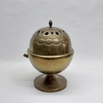 Incensário em metal amarelo, formato esférico, base redonda. Tampo martelado, vasado e lavrado com flores estilizadas. Falta o cabo. Alt. 26 cm.